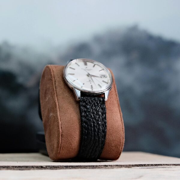 Uhr mit Lederarmband auf einem Uhrenkissen vor nebligen Bergen